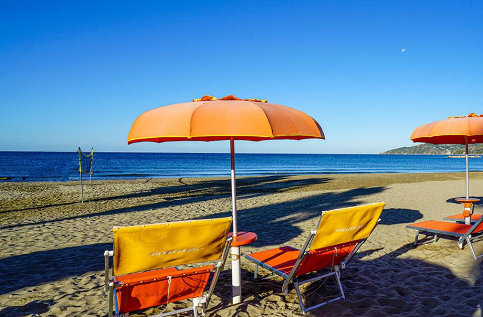 Spiaggia con ombrelloni arancioni, lettini e mare calmo sotto un cielo azzurro.